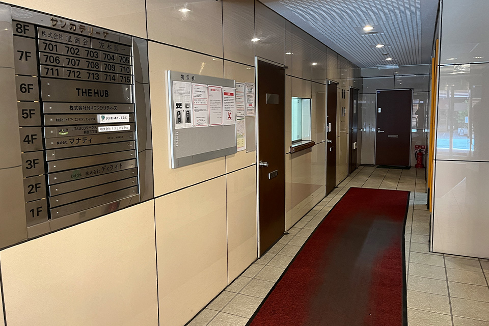 株式会社ディライトの案内板と入口が並ぶ新宿のビル内通路、葬儀関連窓口を示すќе