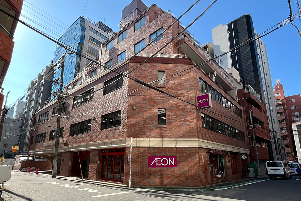 株式会社ディライト本社近くの角地にあるAEON店舗前で葬儀関連の案内を探す通行人