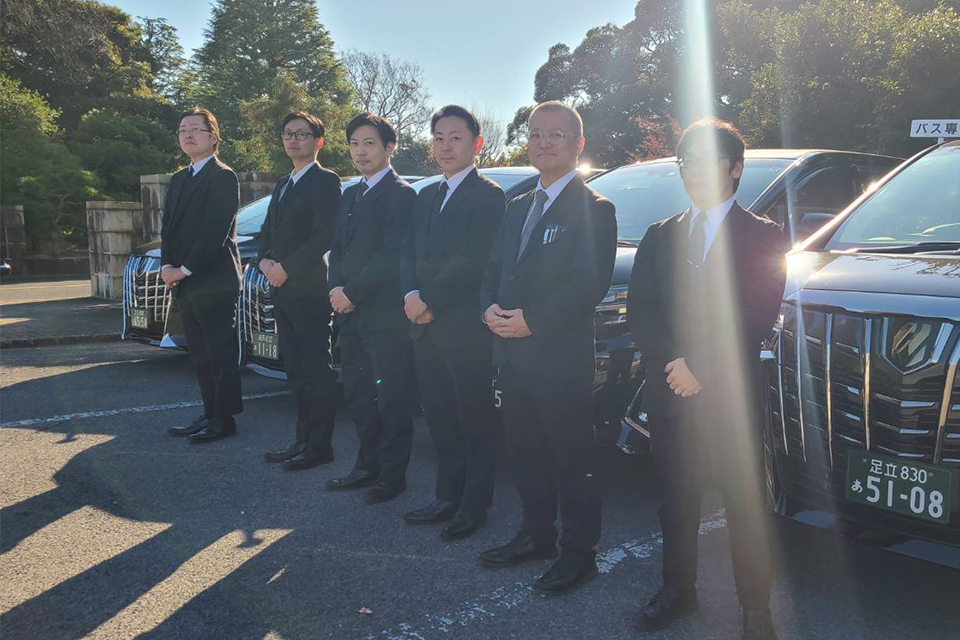 株式会社ディライトのスタッフ6人が搬送用車両の前で葬儀搬送の準備をしている